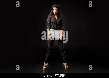 Beau portrait en costume et chaussures de ballet avec ordinateur portable sur fond noir Banque D'Images