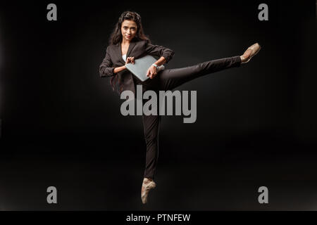 Businesswoman in suit et chaussures de ballet avec ordinateur portable sur fond noir Banque D'Images