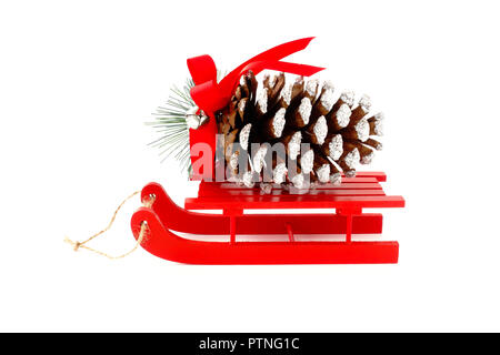 Cône de pin de Noël géant décoré d'argent glitter, Bell et ruban rouge sur rouge traîneau en bois isolé sur fond blanc. Banque D'Images