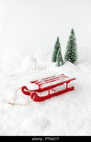 Scène d'hiver avec un traîneau en bois rouge, neige, une boule géante et des sapins. Banque D'Images