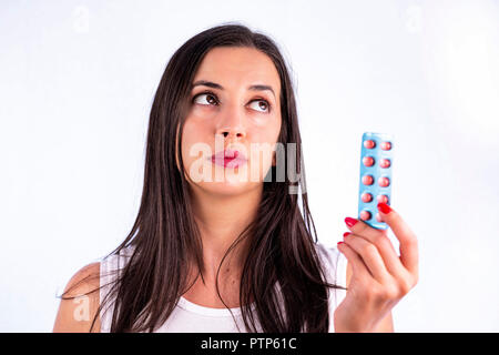 Pilules rouge en blister dans la main de la belle jeune femme à la recherche de l'établissement. L'industrie pharmaceutique mondiale pour des milliards de dollars par année. Studio shot isol Banque D'Images