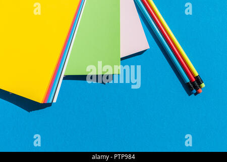 Feuilles de papiers colorés et dynamiques des crayons sur fond bleu Vue de dessus - palette de couleurs Banque D'Images