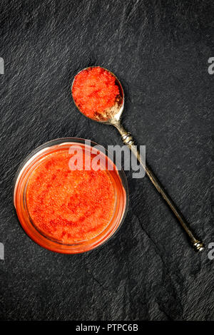 Une photo prise à la verticale de caviar rouge dans un bocal et dans une cuillère, tourné à partir de ci-dessus, sur un fond noir avec copyspace Banque D'Images