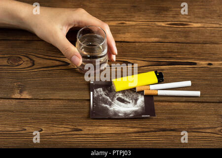 A woman's hand est titulaire d'un verre d'alcool, à côté c'est une photo de l'uzi la grossesse et les cigarettes, la grossesse et le tabagisme, la cigarette Banque D'Images