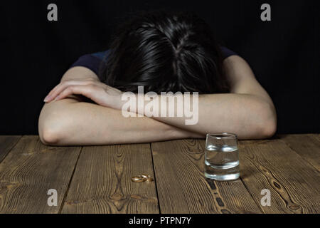 Une jeune fille ivre se trouve sur une table en bois, posé sa tête sur une table, un fond noir, femme l'alcoolisme Banque D'Images