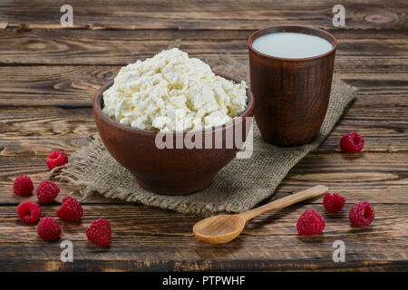 Le fromage cottage et le lait dans clayware sur table en bois, un sac de serviette de table et cuillère en bois Banque D'Images