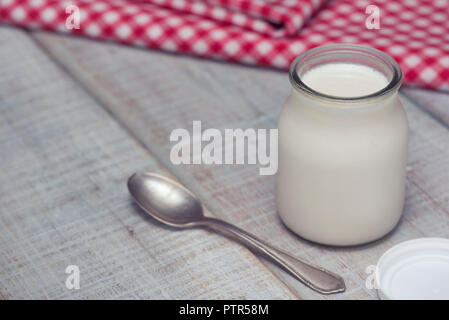 Délicieux et sain des yaourts blancs dans un bocal en verre sur une table en bois blanc. Prêt à manger comme cela, ou l'ajout de fruits, de céréales ou d'écrous. Banque D'Images