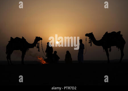 L'image de l'homme extrait traditionnel rajasthani, femmes et chameau avec le feu au lever du soleil à Jaisalmer, Rajasthan, India Banque D'Images