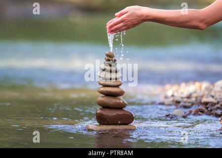 Close-up résumé image de femme part verser de l'eau sur les différentes tailles inégales brun naturel et la forme des pierres comme équilibrée pile pyramide monument Banque D'Images