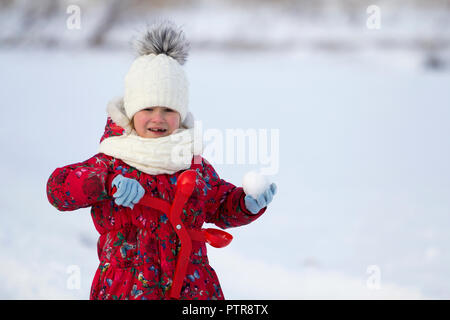 Jolie petite jeune fille drôle enfant édenté dans des vêtements chauds s'amusant jeu de boules de décisions sur l'hiver froid jour lumineux blanc copie floue savs Banque D'Images
