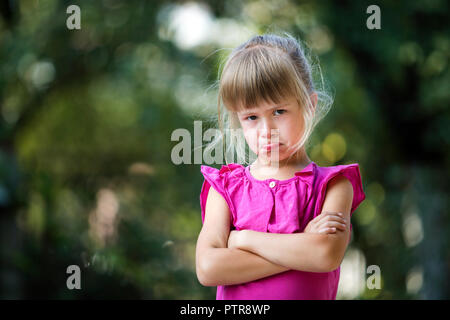 Portrait of pretty funny moody malheureux enfant blonde girl in pink robe sans manches en colère et mécontent sur été floue arbre vert copie Banque D'Images