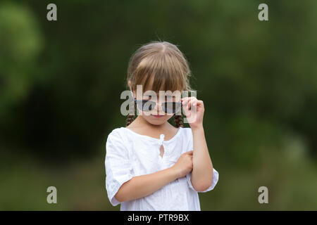 Portrait of cute assez drôle cool à la mode jeune fille en colère insatisfaite moody blonde avec tresses en robe blanche et des lunettes sur floue summ Banque D'Images