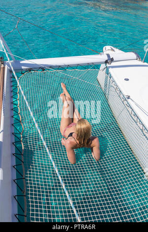 Womanin bronzage bikini et reposant sur un été glaciaire voile croisière, couché dans un hamac de catamaran de luxe près de la plage de sable blanc de Spargi j Banque D'Images