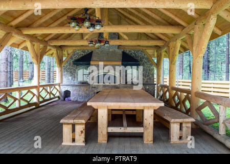Des chambres joliment décorées de l'intérieur ouvert moderne pavillon en bois avec poutres apparentes et murs, table massive, bancs et barbecue cheminée pour big stone Banque D'Images
