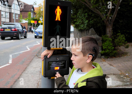 Un jeune garçon qui attend de traverser la route à un panneau de signalisation piéton traversant sur une route dans une zone urbaine avec des voitures approchant le Royaume-Uni KATHY DEWITT Banque D'Images