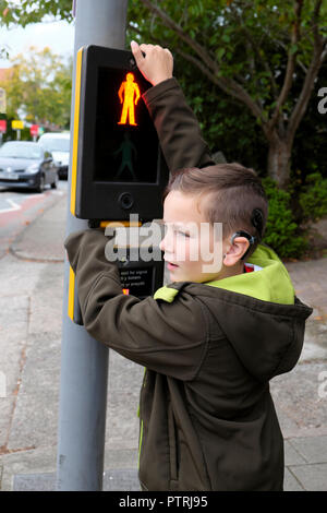 Un jeune garçon en attente de traverser la route à un passage à niveau piéton des feux de circulation dans une zone urbaine UK KATHY DEWITT Banque D'Images