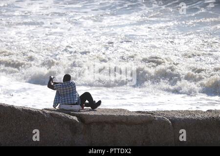 Hastings, East Sussex, UK. 11Th Oct, 2018. Météo France : avec des rafales de vent jusqu'à 30mph mais matin ensoleillé à St Leonards à Hastings. Hauts de 19°C. Homme assis sur un disjoncteur de la mer prend une des selfies le fracas des vagues autour de lui. © Paul Lawrenson, 2018 Crédit photo : Paul Lawrenson / Alamy Live News Banque D'Images