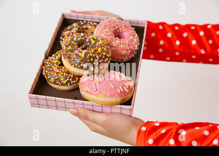 Female hands holding box avec vitrage donuts colorés sur fond clair Banque D'Images