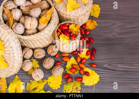 Les noix, églantier et feuilles jaunes sur une surface en bois, des aliments sains à partir de la nature. Concept d'automne fond Banque D'Images