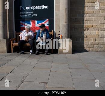 Un couple de personnes âgées s'asseoir sur un siège à l'extérieur de la coopérative de Bakewell, Derbyshire de manger du poisson et frites. Banque D'Images