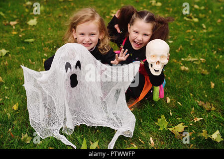 Deux petites filles en costumes de carnaval des sorcières pour l'halloween avec un jouet ghost dans le parc sur un fond de feuillage de l'automne et de l'herbe Banque D'Images