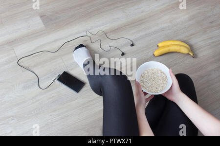 Une fille est assise sur le sol et tenant une plaque avec un faisceau, un téléphone avec un casque, les bananes Banque D'Images