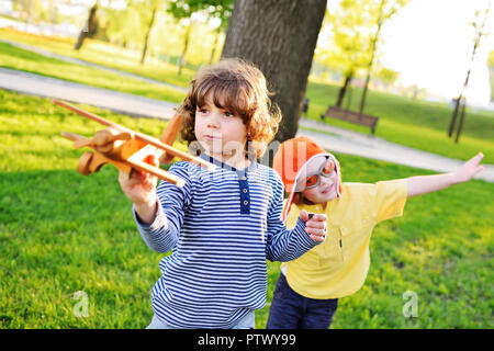 Deux petits enfants de garçons avec des cheveux bouclés jouer un avion jouet en bois dans le parc. Banque D'Images