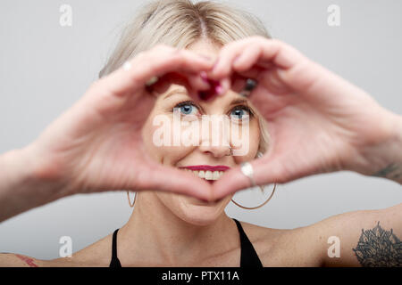 Belle jeune femme faisant une forme de coeur en face de son visage. Banque D'Images