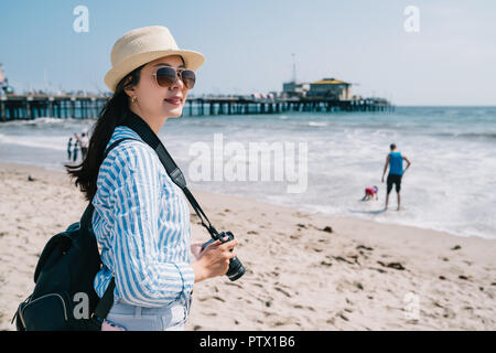 Une jolie femme photographe portant des lunettes de soleil et debout sur la plage Banque D'Images