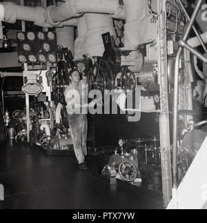 Années 1950, historique, le marin ou une roue tournant lubrification tout en travaillant sous le pont dans la salle des machines d'un navire à vapeur. Une zone de machines complexes et les systèmes de pression wokring ensemble pour faire avancer le navire, le technicien est un membre de l'équipage des navires. Banque D'Images