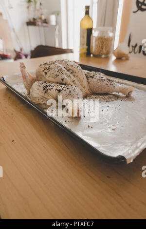 Ensemble le poulet cru être spatchcocked en préparation de torréfaction : hands up portant des gants de manutention de denrées alimentaires à l'aide de ciseaux de cuisine et couteau Banque D'Images