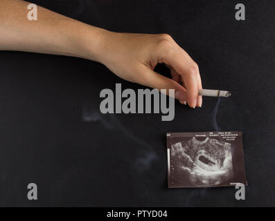 A woman's hand est titulaire d'une cigarette dans le contexte d'une photo de l'uzi de la grossesse, la grossesse et le tabagisme, la gestation Banque D'Images