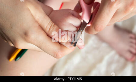 Mère coupe ses ongles dans les mains d'une petite fille, close-up Banque D'Images