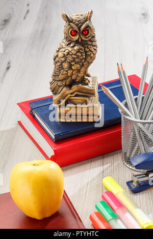 Livres avec statuette de terriers sur le dessus, base métallique avec crayons, agrafeuse, marqueurs de couleur et avec l'ordinateur portable Apple gris jaune sur fond de bois. S Banque D'Images