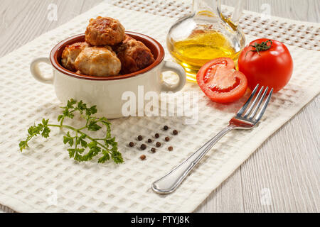 Une viande escalopes dans bol à soupe en céramique, tomates rouges, le flacon en verre avec de l'huile de tournesol, fourchette métallique, branche de persil frais et de poivre noir sur blanc Banque D'Images