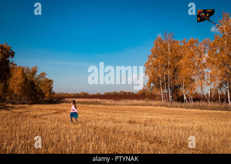 Le concept de famille livestyle et les loisirs de plein air en automne. Une blonde cheerful girl bénéficie de la nature et joue avec un cerf-volant sur une chaude journée ensoleillée d'automne Banque D'Images