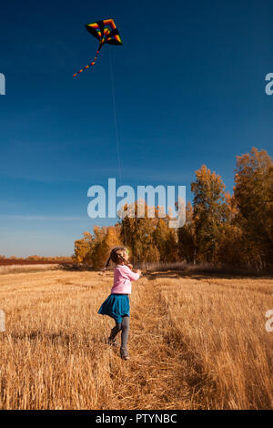 Le concept de famille livestyle et les loisirs de plein air en automne. Une blonde cheerful girl bénéficie de la nature et joue avec un cerf-volant sur une chaude journée ensoleillée d'automne Banque D'Images