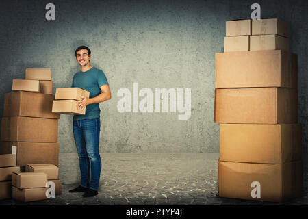 Full Length portrait of happy young man et d'emballage des boîtes de transport prêt à déménager dans une maison isolée sur fond de mur de béton. Banque D'Images