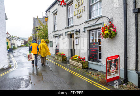 Les touristes visitant la petite ville de Hawkshead dans le lake district se font attraper dehors dans une forte pluie douche Banque D'Images