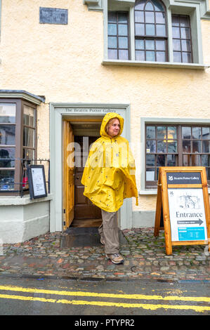 Femme leavingthe touristiques Beatrix Potter Gallery de Hawkshead, Cumbria en un jour pluvieux vêtu d'un poncho. Banque D'Images