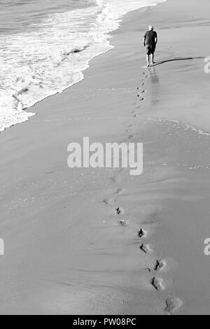 Homme marchant le long de la mer laissant derrière l'empreinte à la plage de Bournemouth - monochrome noir et blanc Banque D'Images