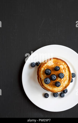 Crêpes aux bleuets sur une plaque ronde blanche sur fond de bois noir, vue du dessus. Copier l'espace. Mise à plat, les frais généraux, d'en haut. Banque D'Images