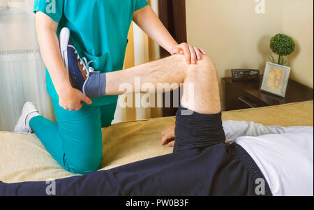 Physiothérapeute faisant des exercices de récupération de la jambe d'immobilisation du patient de sexe masculin à la maison. Les gens, de la santé et de récupération concept. Banque D'Images