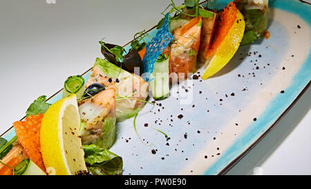 Rouleaux de poisson frit avec des herbes et légumes sur plaque bleue Banque D'Images