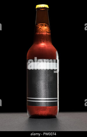 La bière dans un flacon de verre brun sur une plaque en ardoise. Fond noir solide. Orientation verticale. Banque D'Images