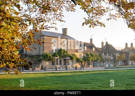 Cotswold boutiques / maisons face au village vert dans l'automne tôt le matin du soleil. Broadway, Cotswolds, Worcestershire, Angleterre. Banque D'Images