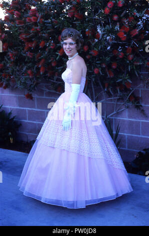 1962, l'Amérique, aller au bal....une jeune femme portant une longue robe rose à froufrous représente une photo contre certaines fleurs rouge dans son arrière-cour avant de participer à la prom, une danse traditionnelle fin de terme pour nous les élèves du secondaire.Dans les années 50 et 60, le bal était plus d'un couple, l'événement, où un garçon lui demande une fille d'être sa date et serait son escorte après avoir sélectionné son jusqu'à son domicile et avoir beaucoup de photo prises ! Banque D'Images