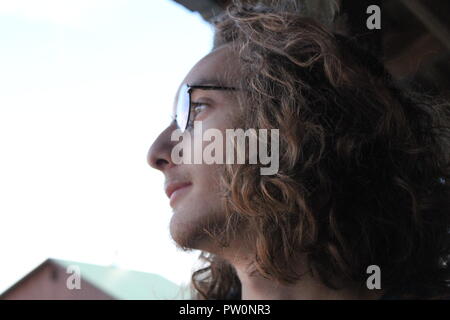 Heureux jeune homme avec des lunettes et des cheveux longs regards dans la distance Banque D'Images