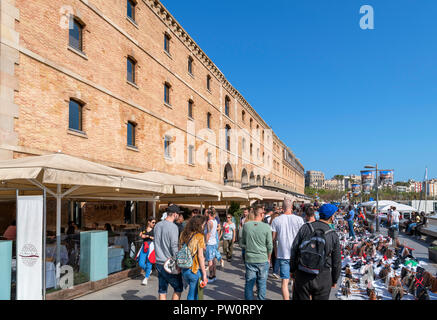 Les vendeurs de rue et les touristes sur Moll del Dipòsit dans le Port Vell (vieux port) avec le Museu d'Història de Catalunya à gauche, Barcelone, Espagne Banque D'Images