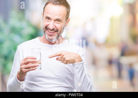 L'âge moyen hoary senior man drinking glass of water sur fond isolé très heureux pointant avec la main et des doigts Banque D'Images